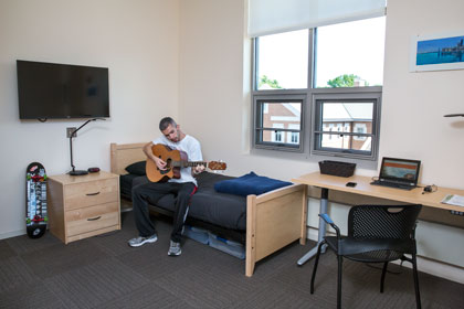 man playing guitar while sitting on his bed in his bedroom