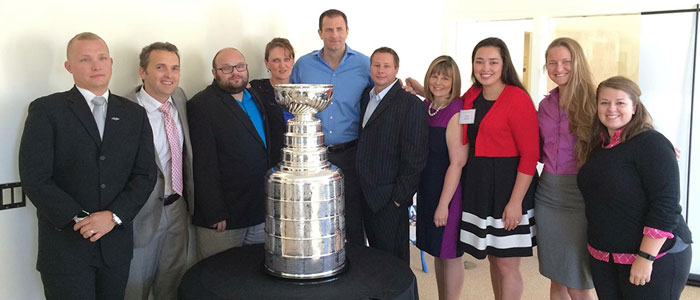 10 staff members posing around the Stanley Cup trophy